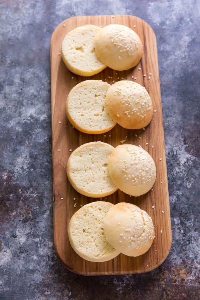 A deep wooden cutting board with hamburger buns sliced open