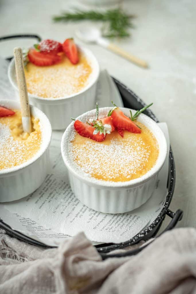 three white ramekins with custard on a tea tray.