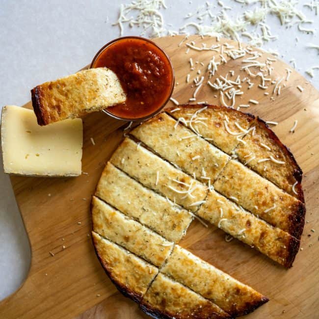 cauliflower breadsticks on a pizza board with marinara dipping sauce