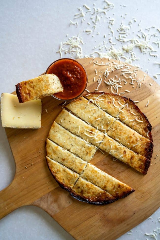 cauliflower breadsticks on a pizza board with marinara dipping sauce