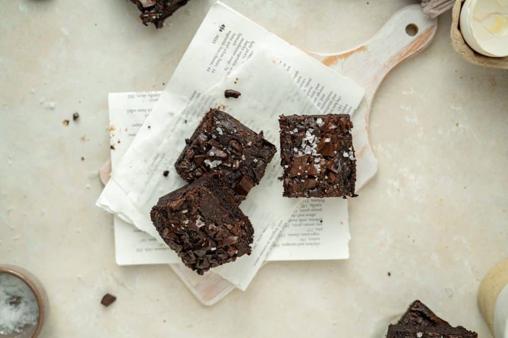 Keto Avocado Brownies Brownies on a white wood cutting board with extra flakey salt.