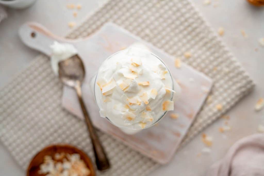 A mini cutting board with a cup of coconut yogurt and a silver spoon 