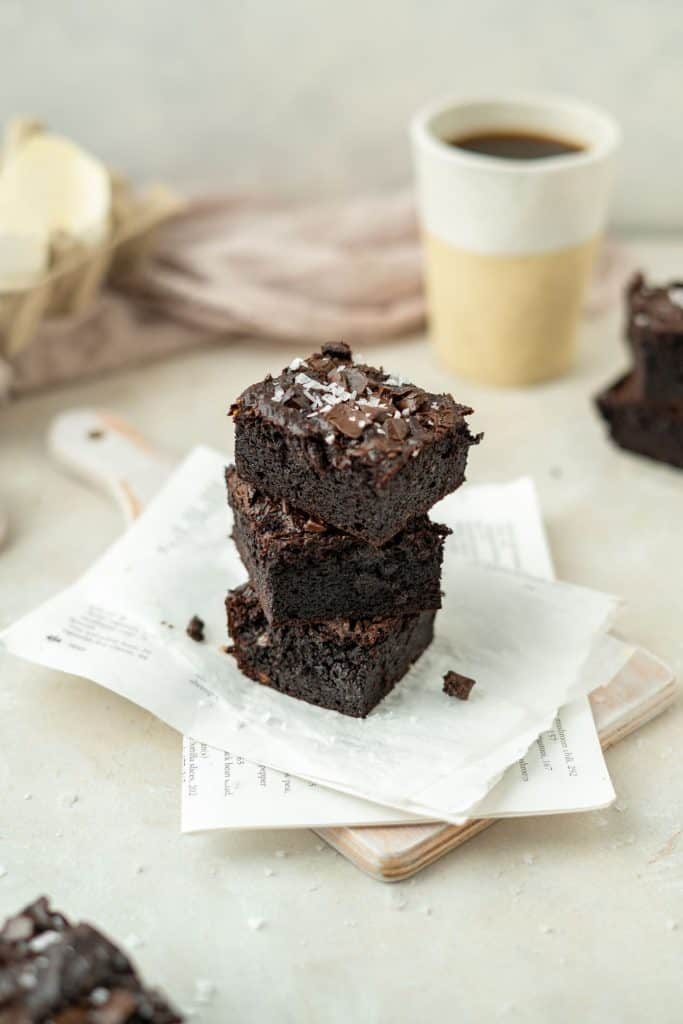 Keto Avocado Brownies Three brownies stacked with a cup of coffee nearby.