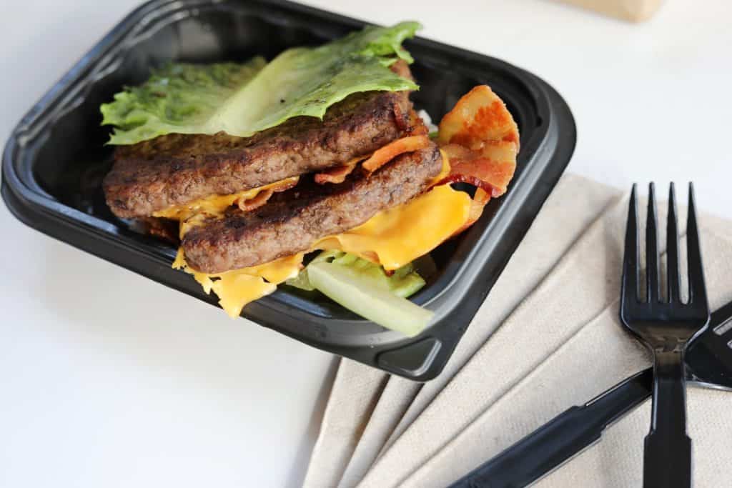 A bun-less burger in a togo clamshell with silverware