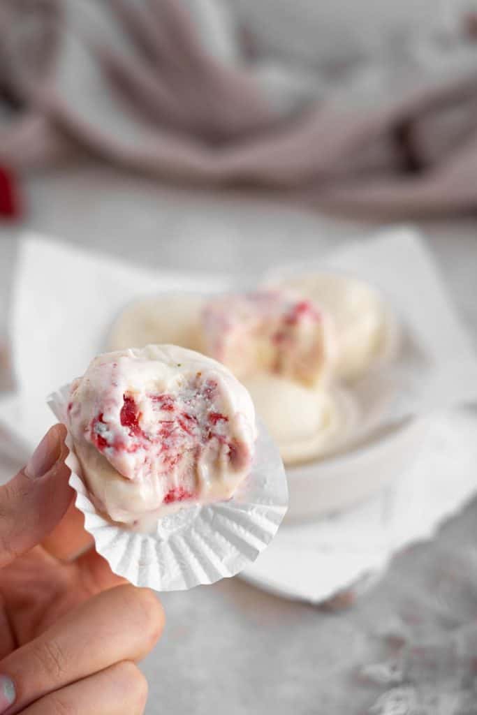 Keto Cheesecake Fat Bombs A hand holding strawberry cheesecake fat bombs with a white cupcake liner