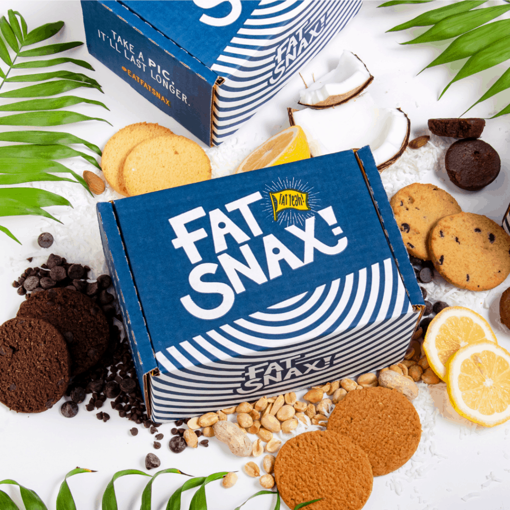 A big box of Fat Snax cookies surrounded by cookies, chocolate chips, peanuts, coconut, and lemon slices