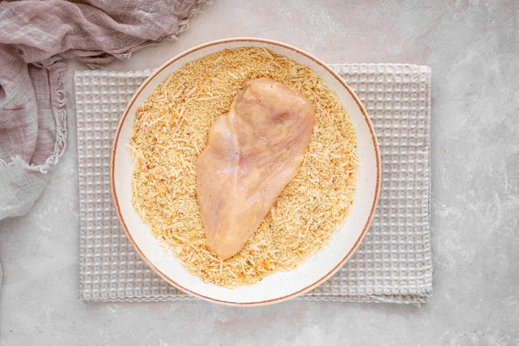 keto chicken parmesan placing a chicken breast in the dry mixture