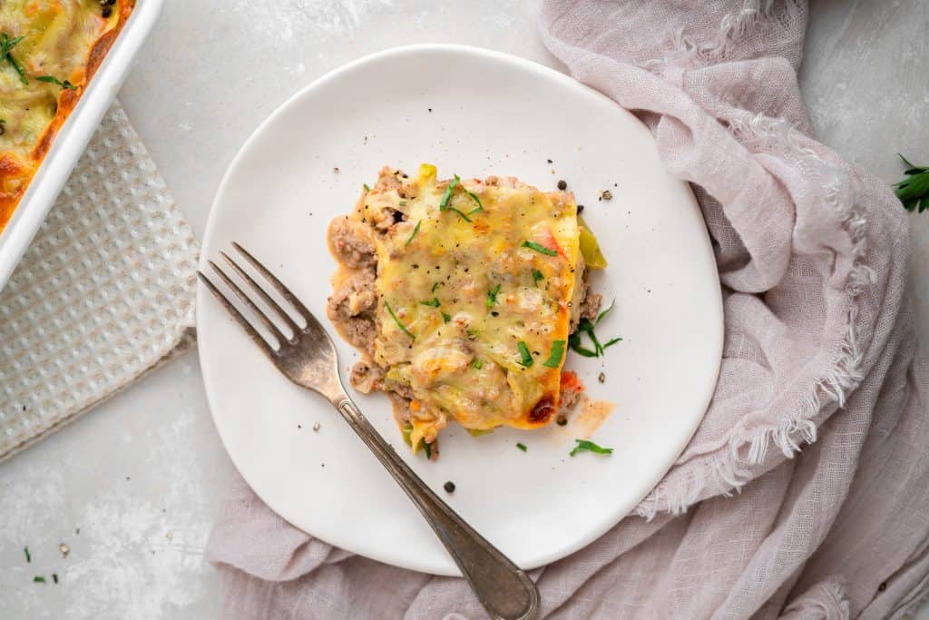 A white ceramic plate with a slice of golden brown cheesesteak casserole