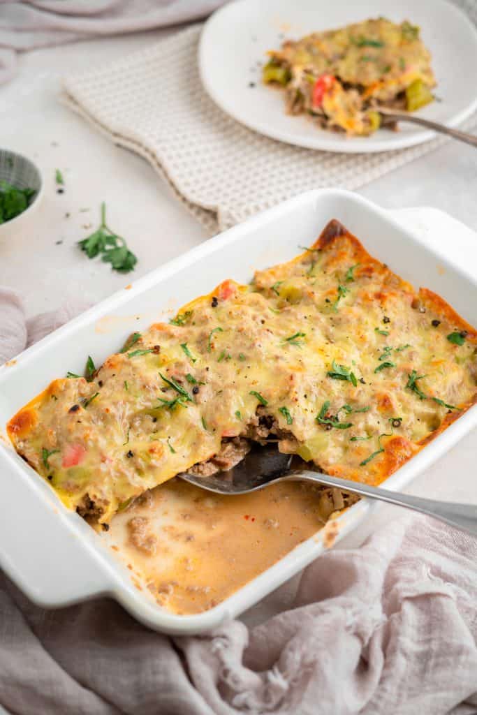 A soft pink hand towel next to a casserole dish of philly cheesesteak casserole