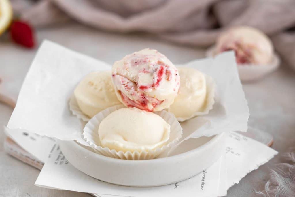 Four cheesecake fat bombs atop parchment paper in a shallow dish