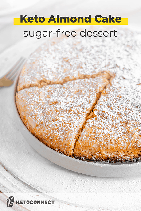 Whole almond flour cake sitting on a plate with a fork. A piece is cut out and it is top with powdered sugar