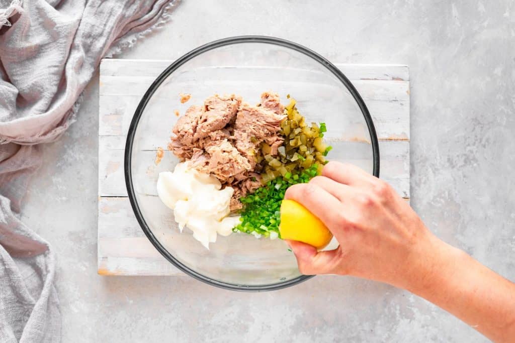 Overhead shot of all the ingredients in a glass bowl with lemon being squeezed in