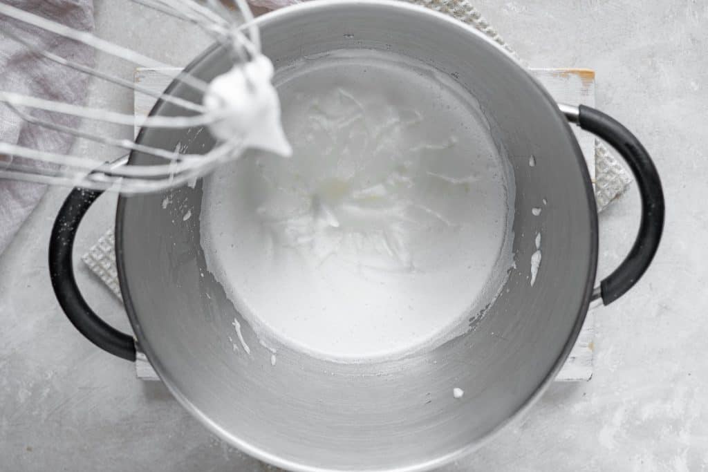 A metal bowl with beaten egg whites with a whisk mixer coming out of it