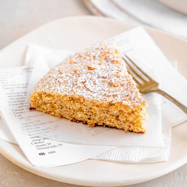 A single piece of Almond Cake sitting on a plate with a fork next to it.