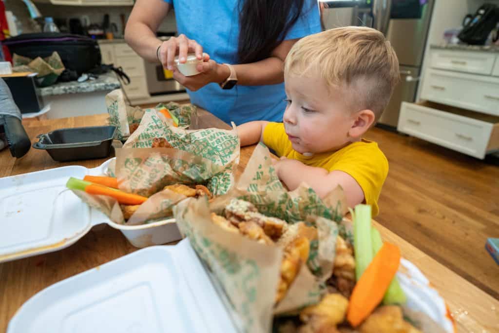 woman and her toddler eating chicken wings from takeout boxes