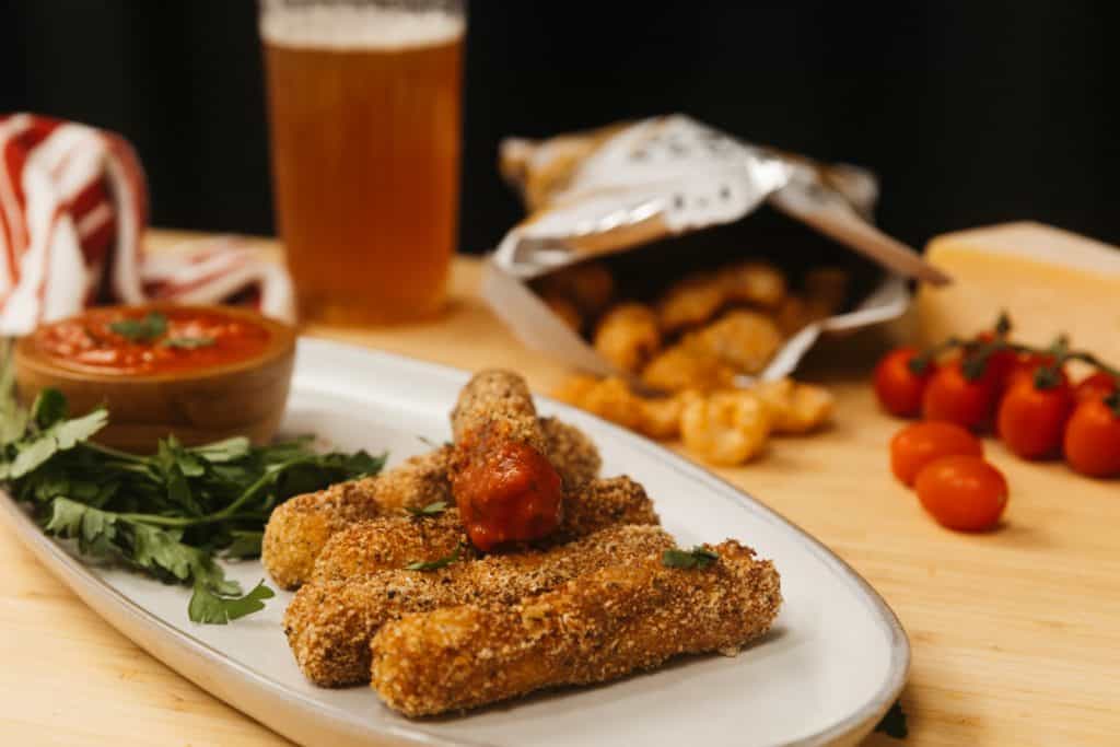 keto mozzarella sticks keto mozzarella sticks on a plate with dipping sauce and tomatoes in the background