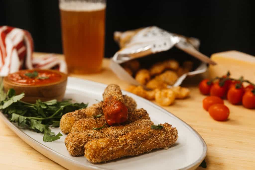 keto mozzarella sticks on a plate with dipping sauce and tomatoes in the background