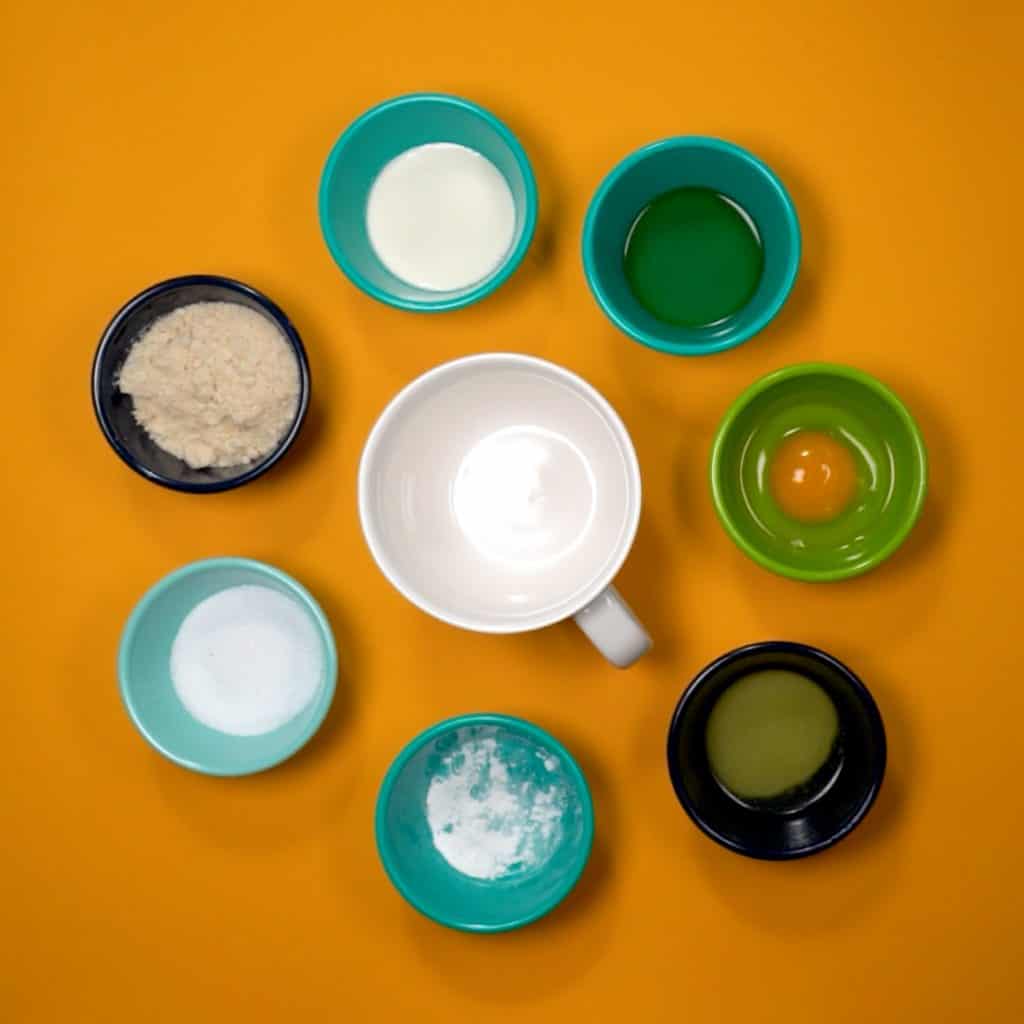 keto Mug Cake ingredients in small bowls being added to a coffee mug