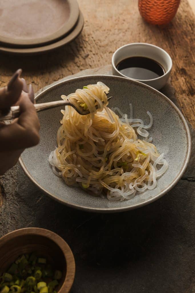 Miracle Noodle Reviews Miracle noodles in a bowl with soy sauce on them and off to the side. A fork dipped in pulling noodles out.