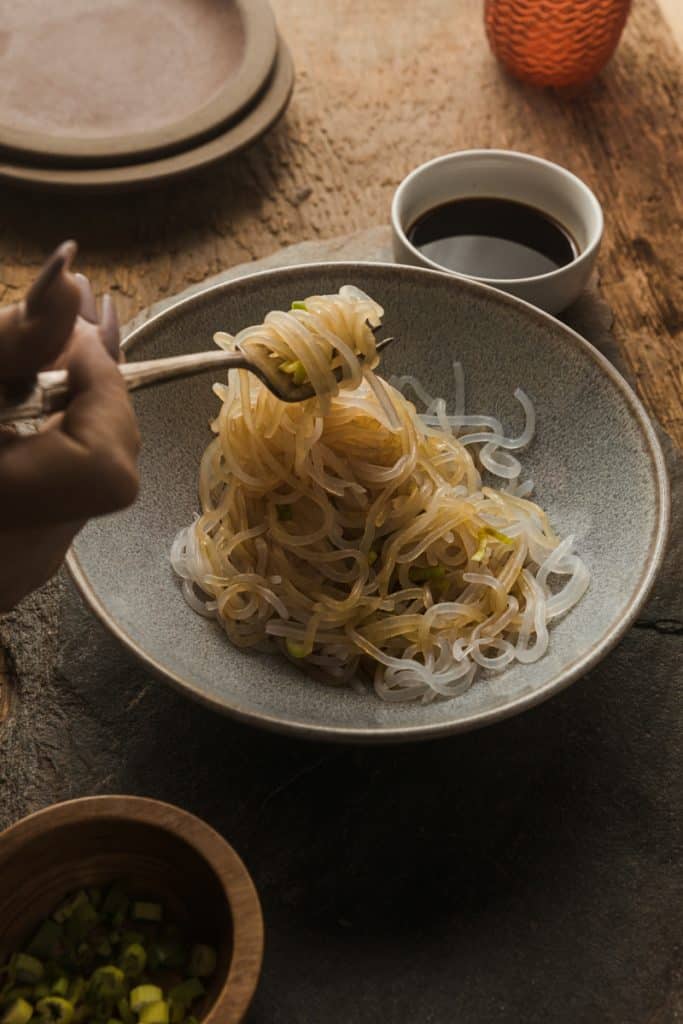 Miracle noodles in a bowl with soy sauce on them and off to the side.  A fork dipped in pulling noodles out.