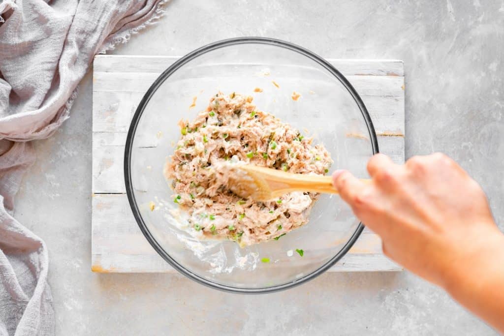 Keto Tuna Salad overhead shot of a wooden spoon mixing all of the ingredients for tuna salad together in a glass bowl