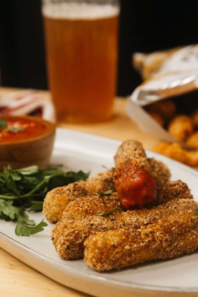 mozzarella sticks on a plate with sauce and beer in the background