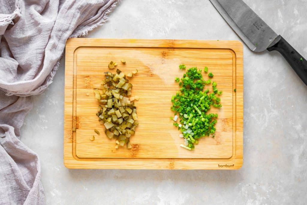 Overhead shot of pickle and green onion laid out on a cutting board with a knife beside it.