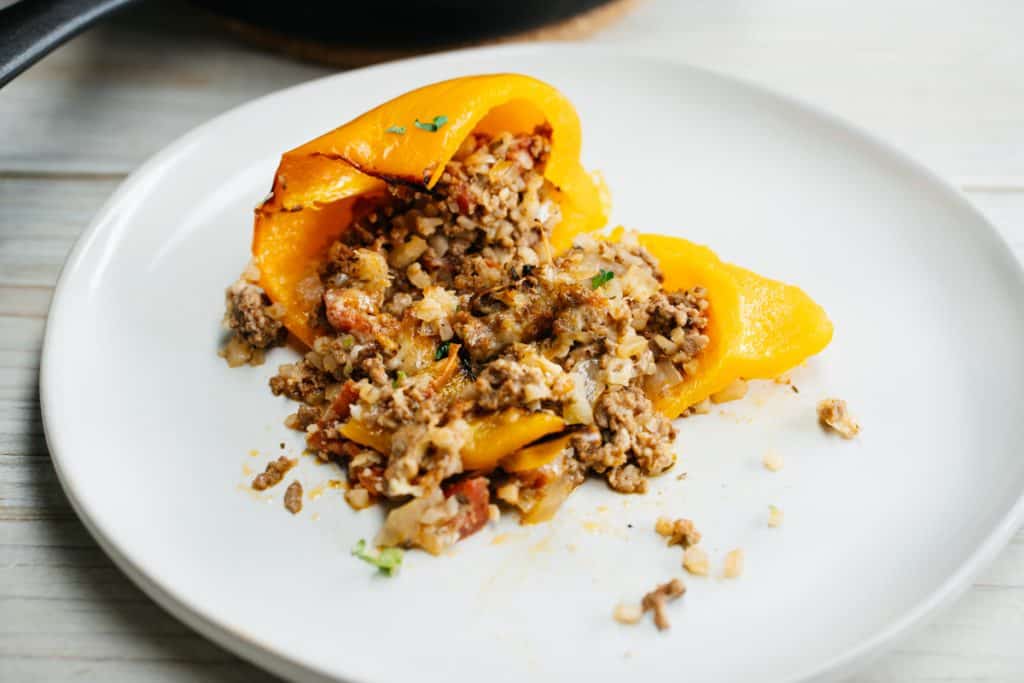 keto stuffed peppers A stuffed pepper on a white plate that has been cut open