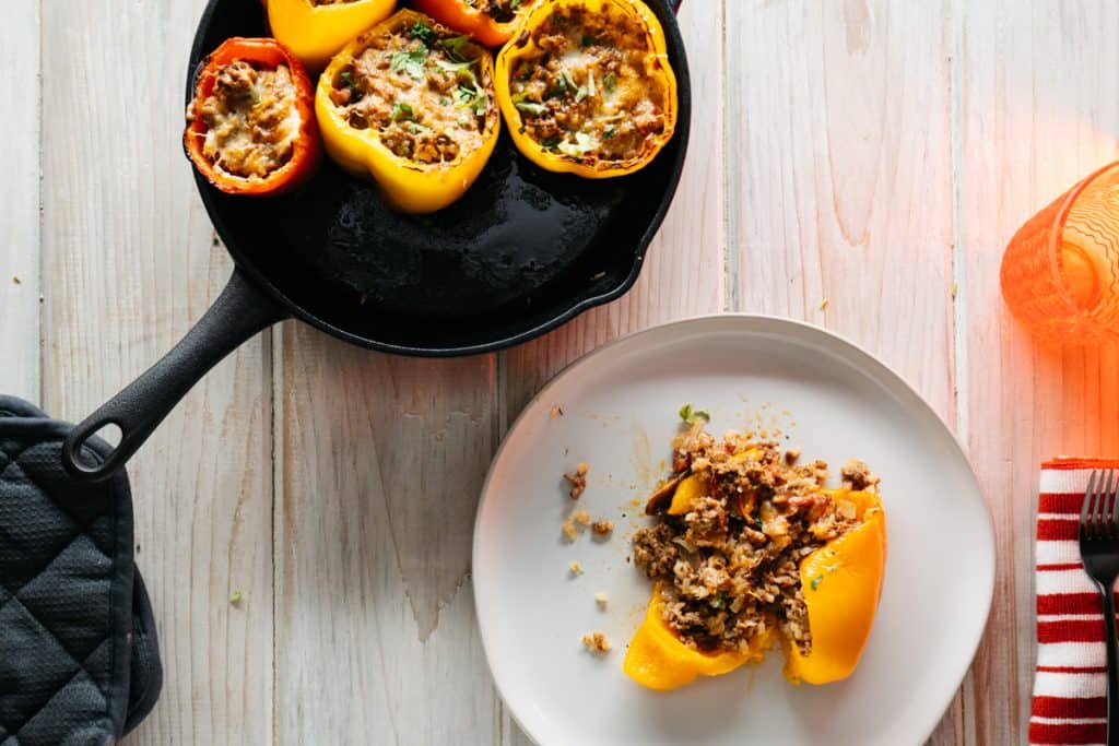 A plate with one keto stuffed pepper on it and several in a pan next to the plate