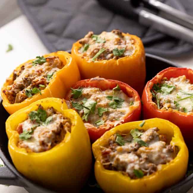 Keto Stuffed Peppers in a cast iron pan with some tongs in the background