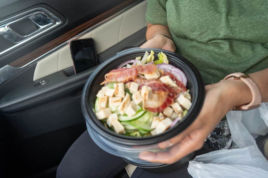 A salad in a bowl with alot of lunch meat being held in a car