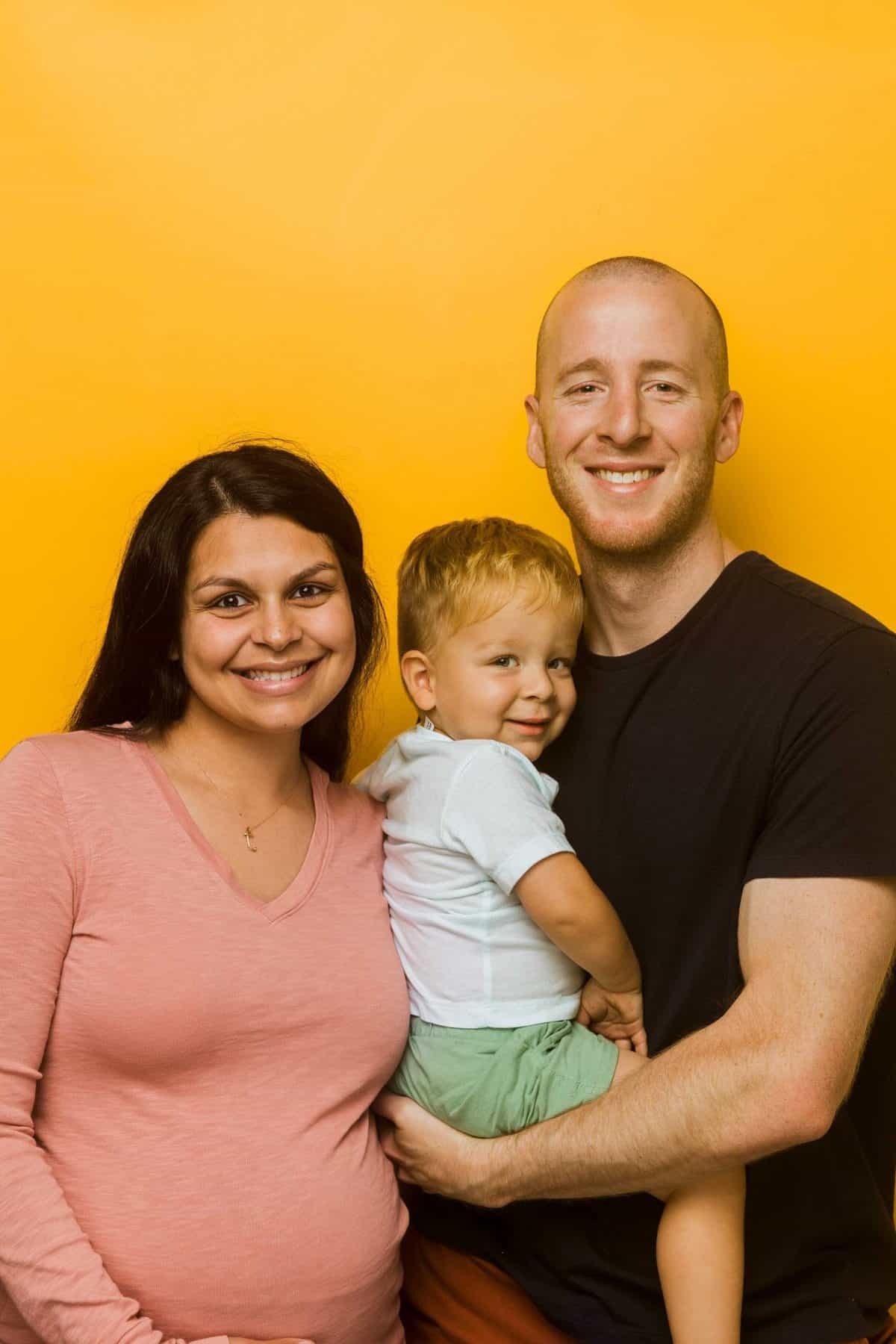 matt and megha and theo in front of orange background