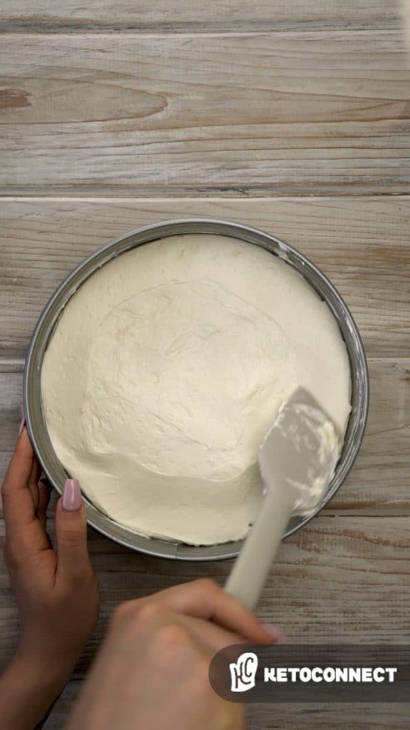 keto no bake cheesecake Overhead shot of filling being added to the crust of no bake cheesecake