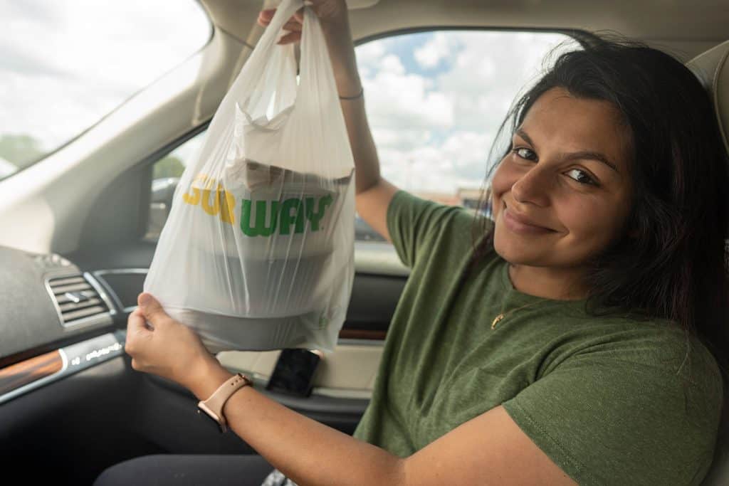 Megha holding up a bag of subway food in a car