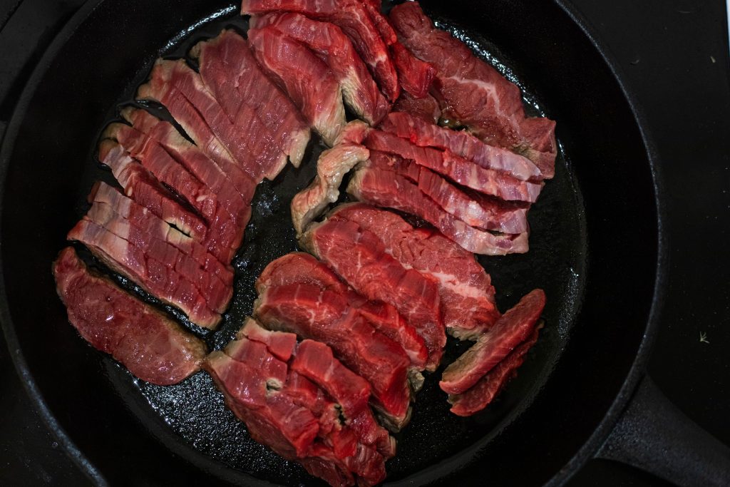 Steak cooking in a skillet with little ribbons of fat throughout 