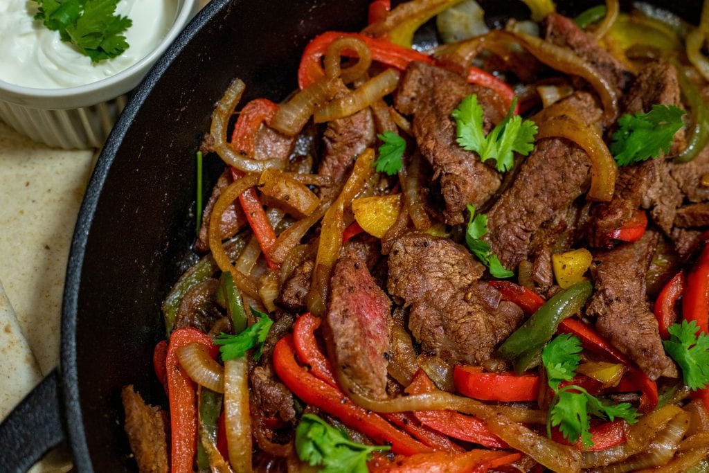 Keto fajitas served up next to a ramekin with sour cream and low carb tortillas. 