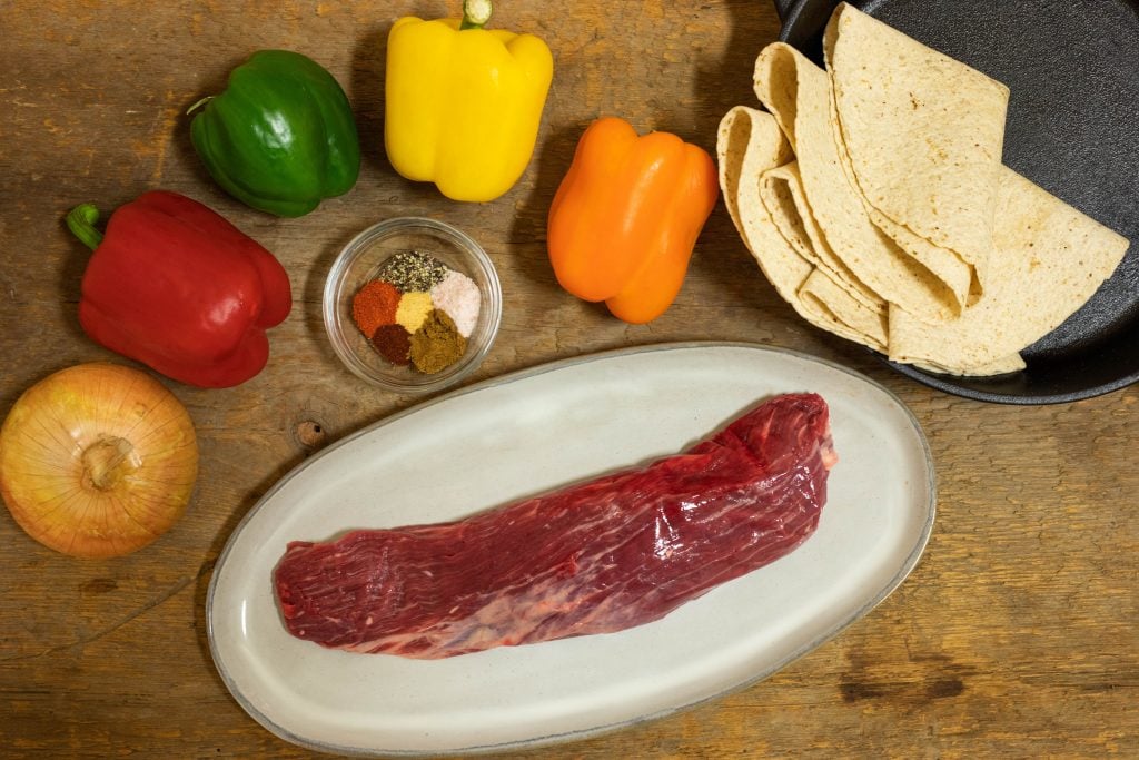 All the ingredients to make keto fajitas placed on an aged wooden table 