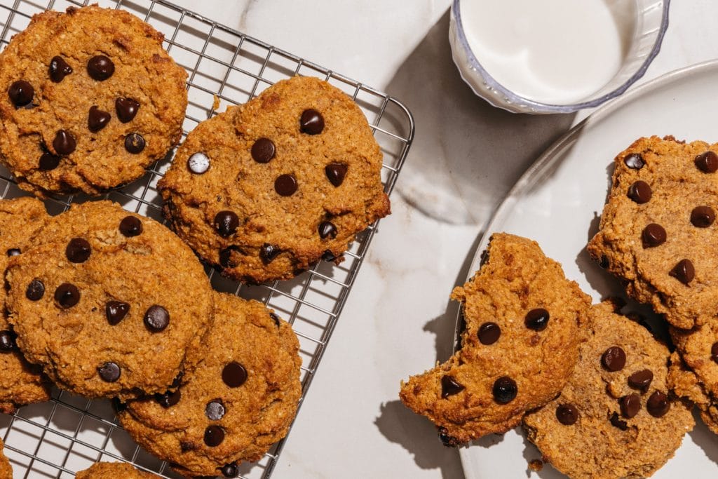 keto pumpkin chocolate chip cookies on a cooling rack with a glass of milk