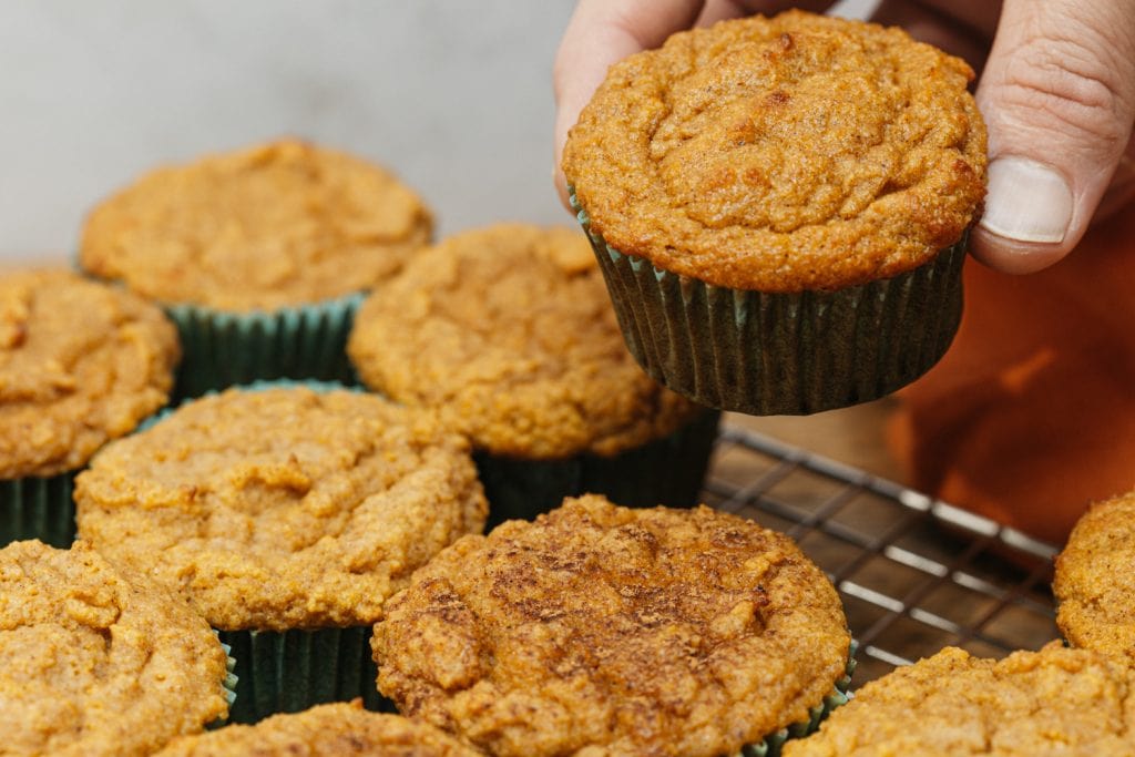 keto pumpkin muffins cooling rack filled with muffins and a man grabbing one
