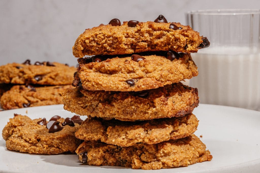 cookies stacked on the table with a glass of milk in the background