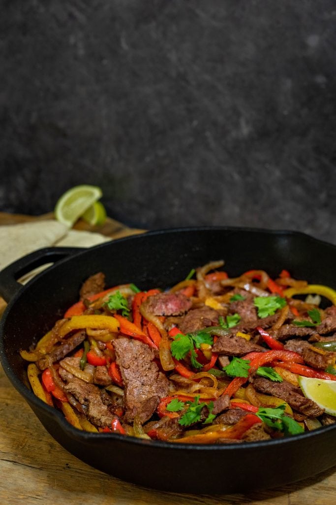 A cast iron skillet placed on the table full of sautéed steak and vegetables. 