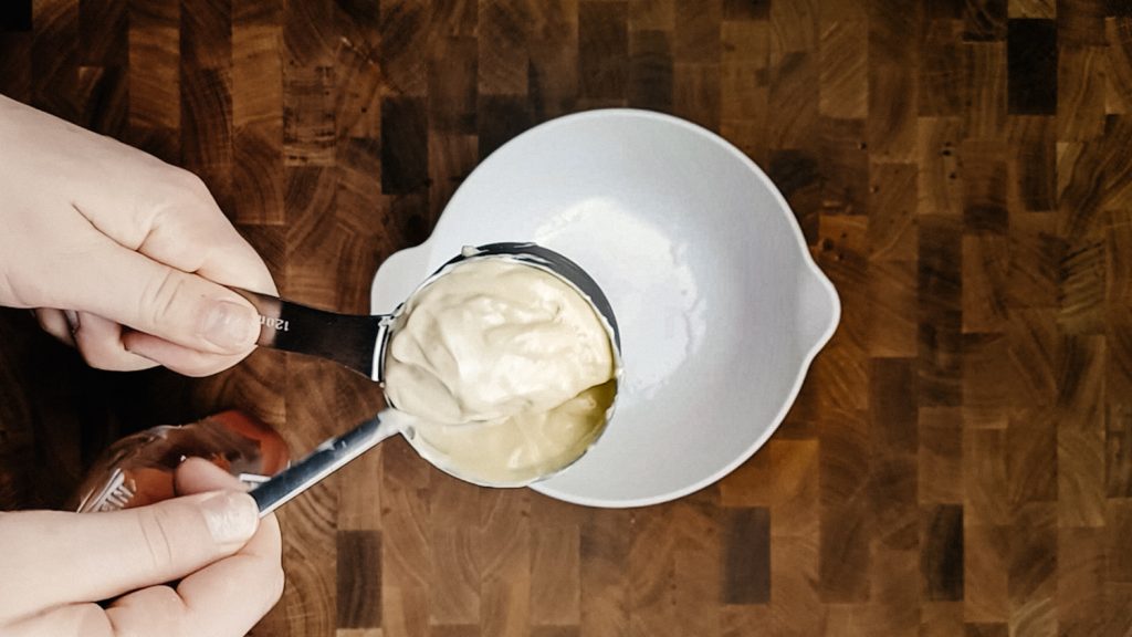 Scooping mayo into a white bowl