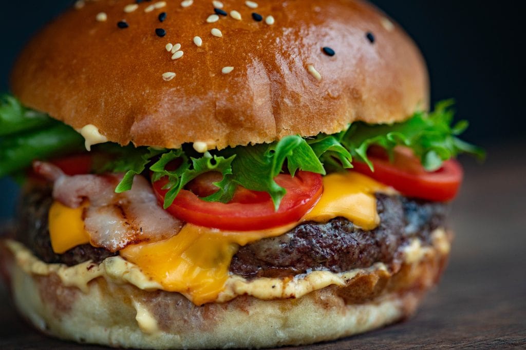 A burger with melted cheese, bacon, tomato, and lettuce. 