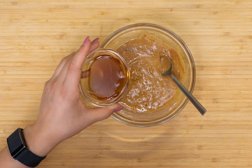 woman adding maple syrup to the peanut butter balls dough