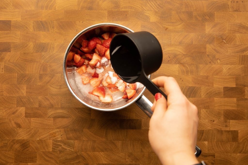 adding sweetener and water to the strawberries