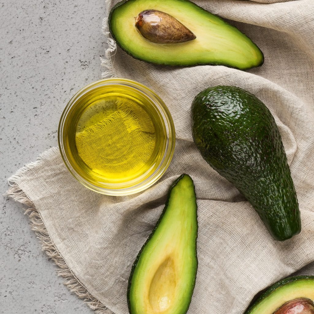 halves and whole avocadoes and bowl of oil