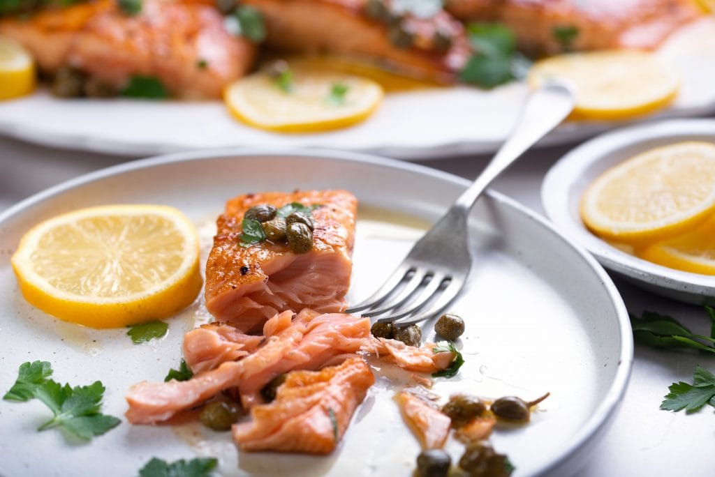 eating pan fried salmon with fork on the white plate